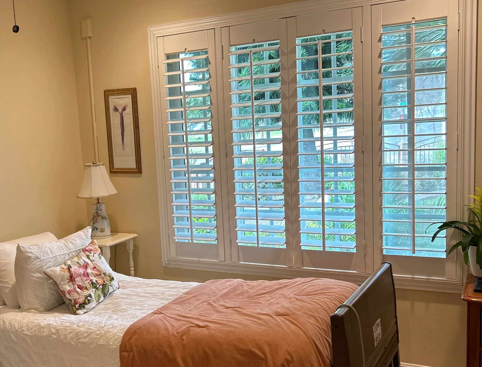 Private bedroom at La Casita Residential Care with an adjustable bed, warm bedding, plantation shutters, and residential furnishings