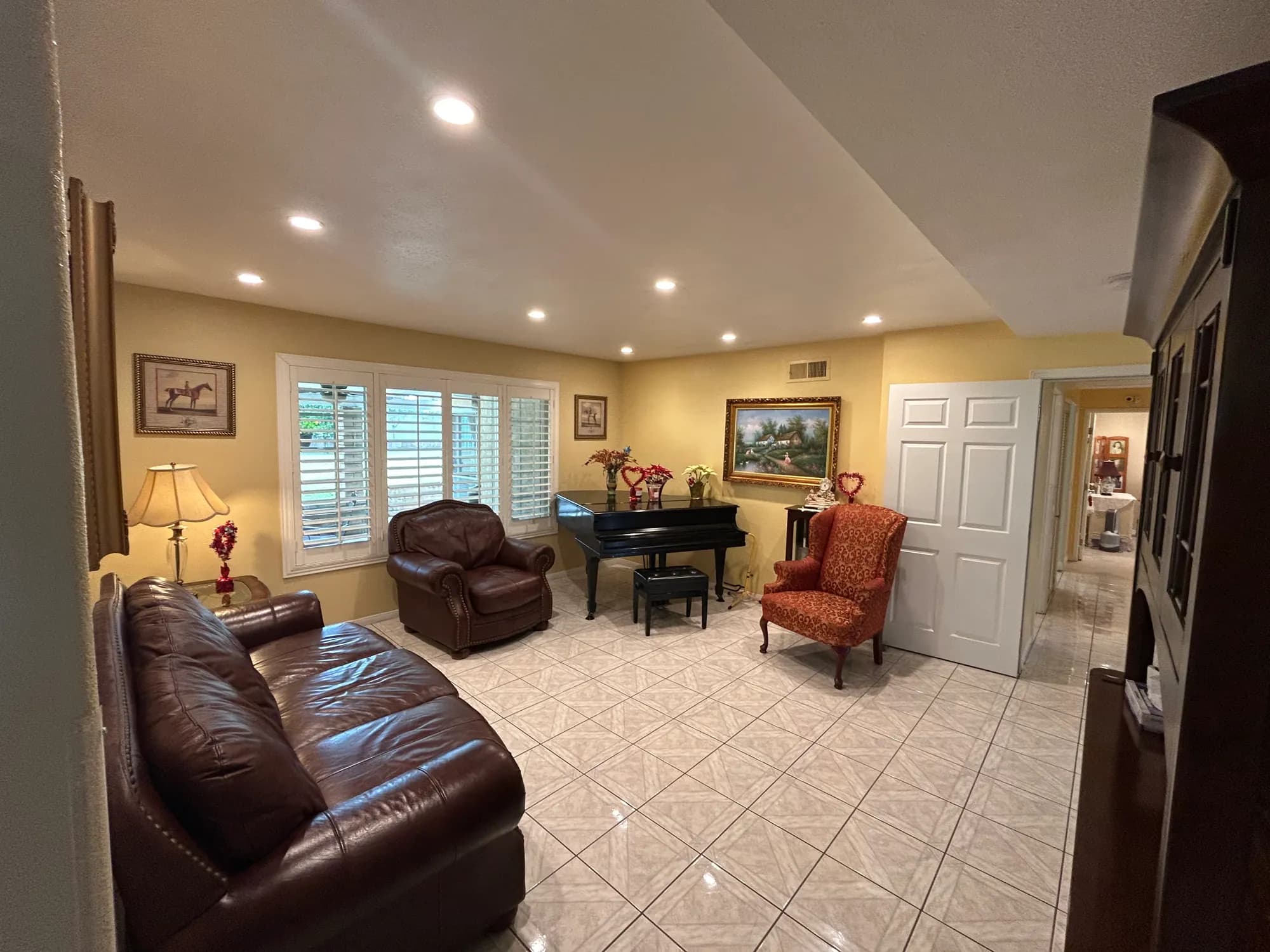 A spacious sitting room with a leather sofa, a grand piano, and framed landscape paintings